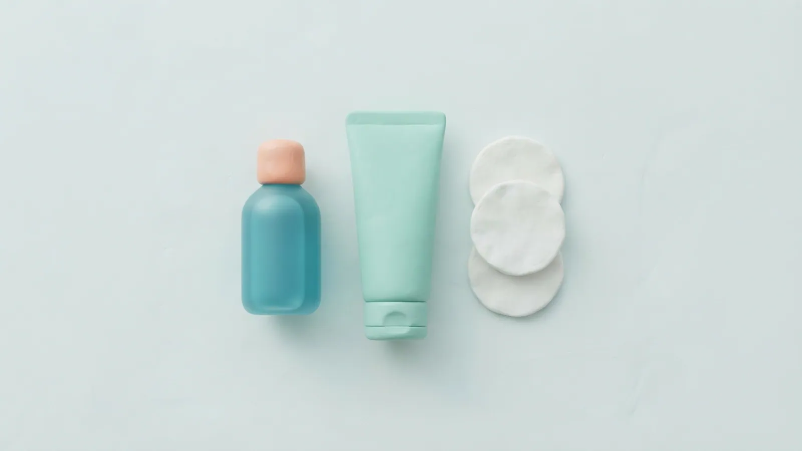 An overhead flat lay of a plain health kit with unlabelled tube, bottle, and pads.